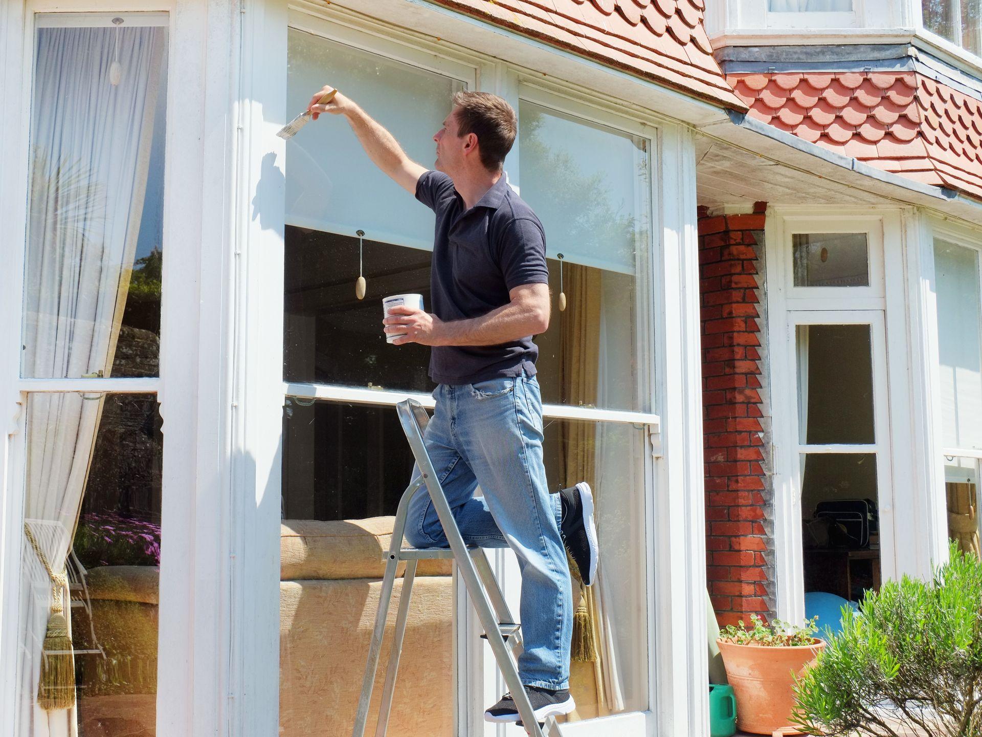 Schilder schildert een raamkozijn aan de buitenkant van een woning